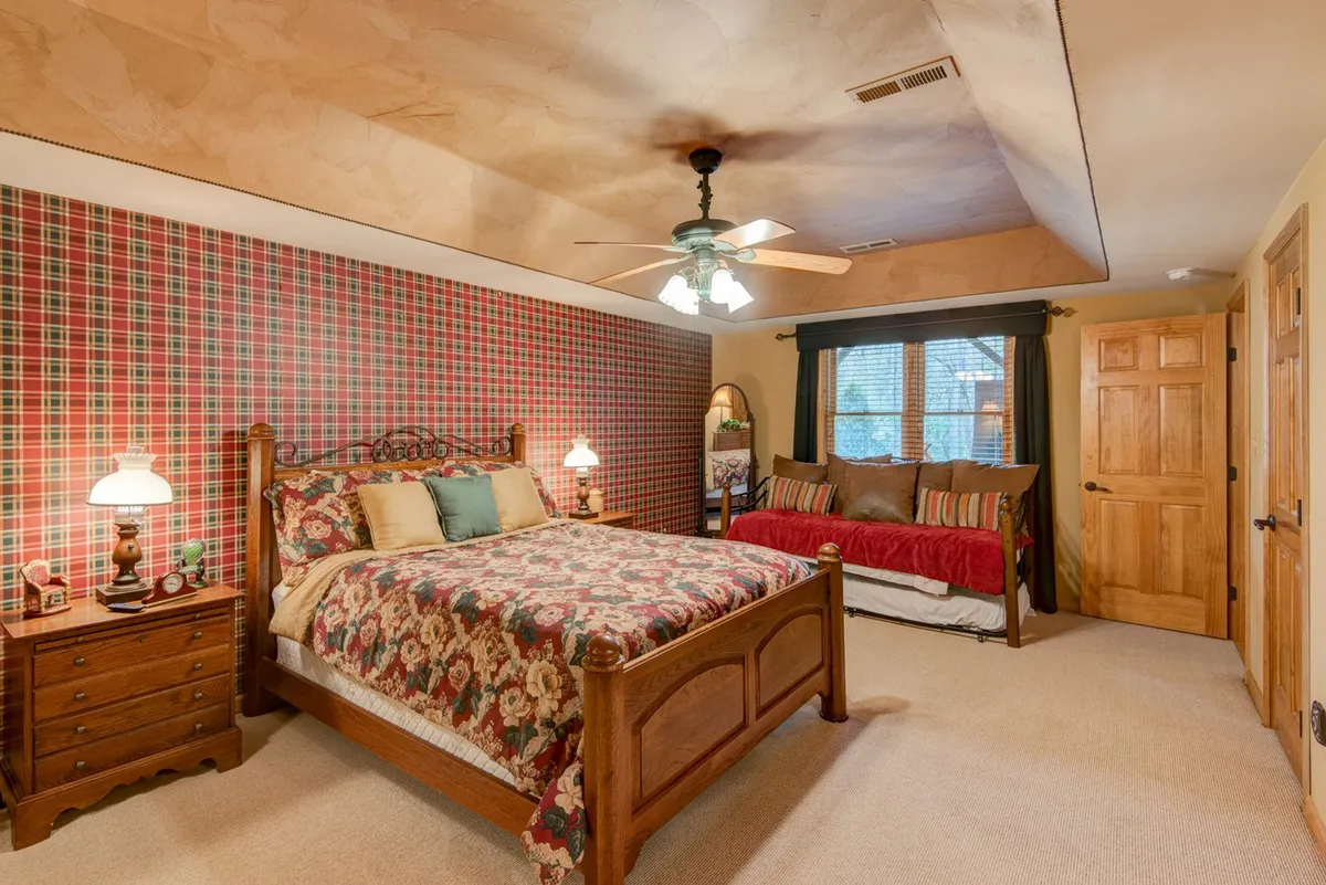 A welcoming bedroom with a plaid accent wall, floral bedding, classic wooden furniture, and a daybed adorned with striped pillows. The space feels ideal for kids or friends to share stories, evoking a sense of warmth and togetherness.