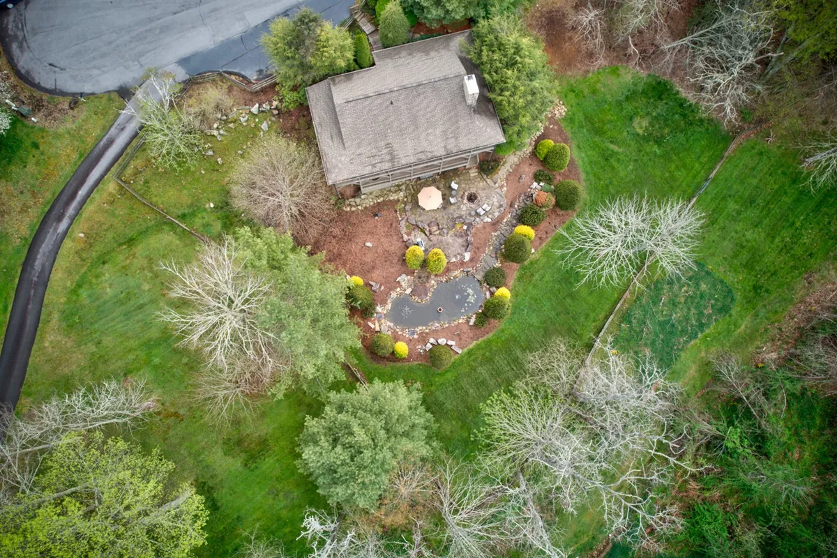 A beautiful view of the house situated next to a landscaped garden pond, surrounded by lush greenery and comfortable outdoor seating. This setting merges the tranquility of nature with inviting spaces for relaxation or outdoor dining, evoking the peaceful mountain escape described in the section.