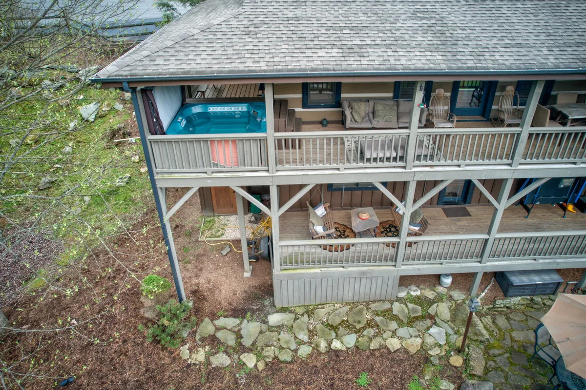 This image shows a casual outdoor space with a hot tub, comfortable patio seating, and a natural stone pathway. The setup hints at both relaxation and social gatherings, complemented by lush greenery and open sky above.