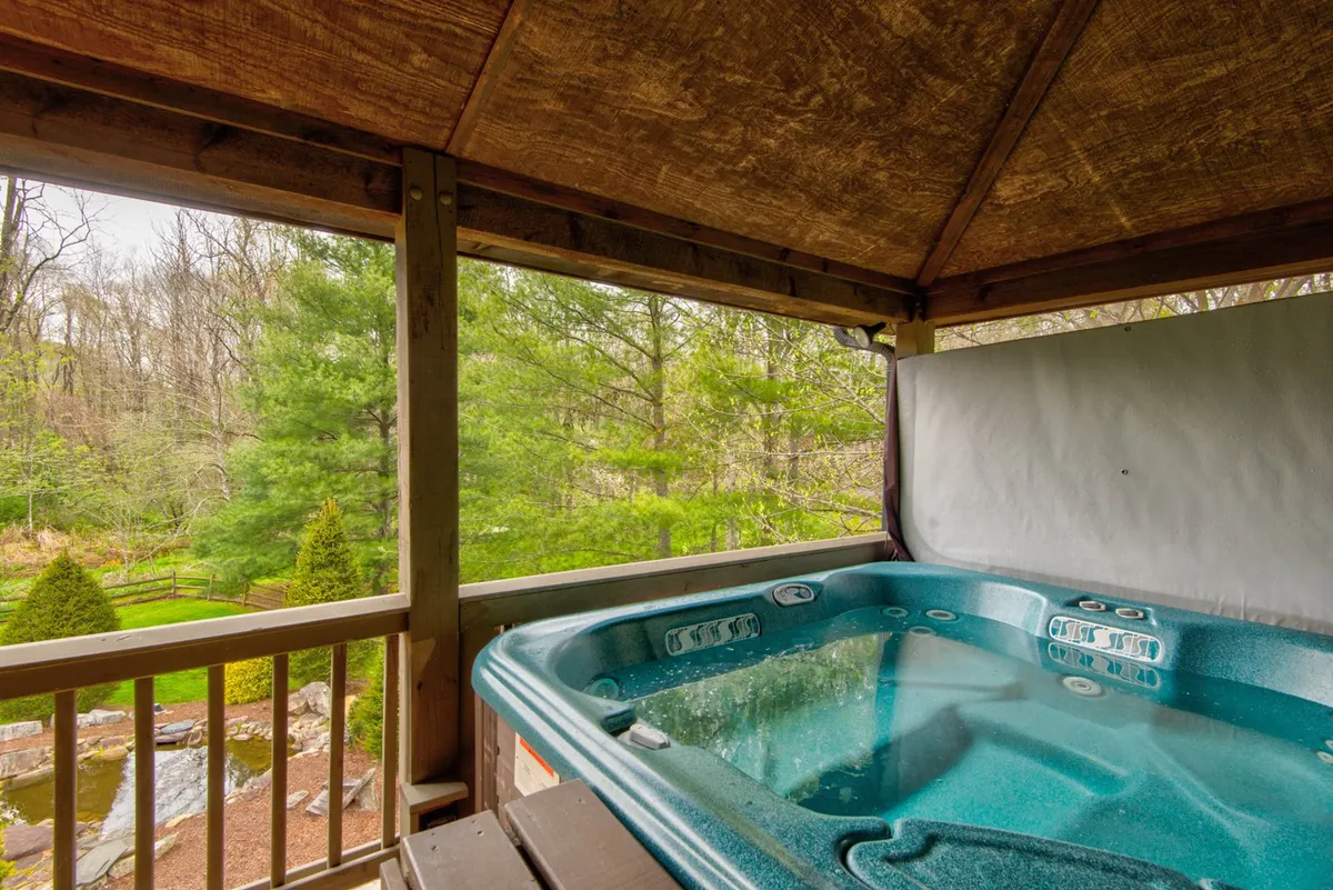 A secluded hot tub is tucked beneath a wooden structure, embraced by natural greenery. The inviting scene offers a private space for soaking, socializing, and enjoying mountain views and fresh air.