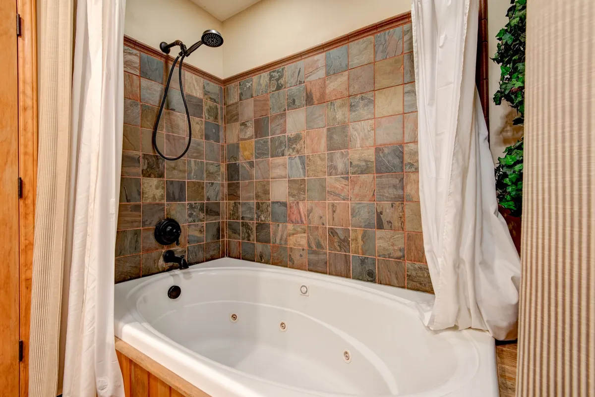 A serene bathroom highlighted by a bathtub, textured tile walls, and a modern shower fixture. The tranquil ambiance suggests a spa-like retreat, perfect for unwinding with a soothing soak after outdoor excursions.