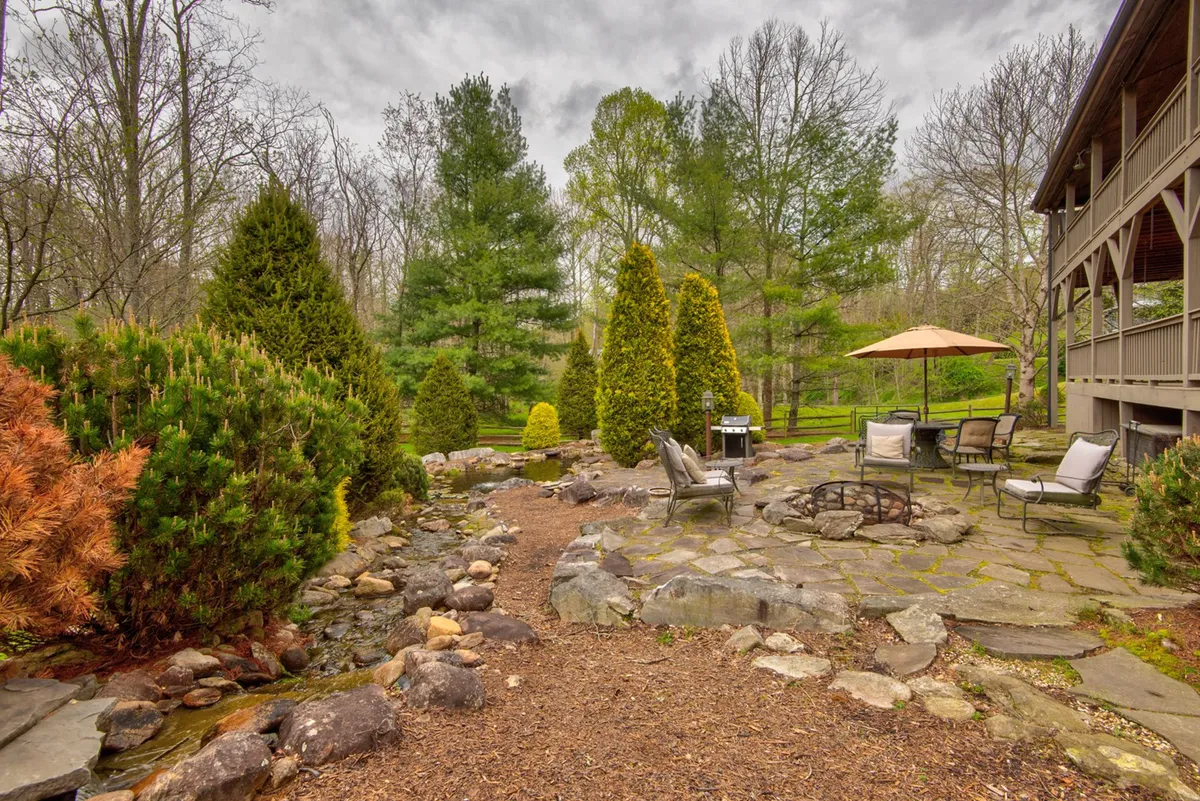 This image features an outdoor stone pathway leading to a fire pit and a cozy seating area nestled among vegetation. The scene is set for relaxing, entertaining, or enjoying evenings by the fire—perfect for family gatherings or roasting marshmallows under the stars.