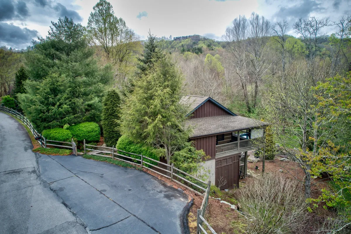 This exterior shot provides a view of the house framed by surrounding trees, a visible fence, and a nearby roadway. The image conveys a sense of spaciousness and connection to the outdoors, with hints at a safe, expansive yard for play and exploration.