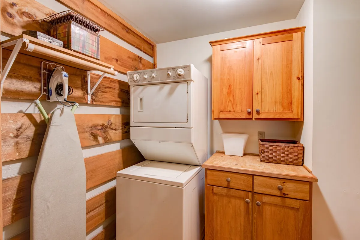 A dedicated laundry area with a washing machine, dryer, wooden cabinets, and ironing board. The practical set-up offers convenience for guests, helping them feel at home and prepared for extended stays or seasonal adventures.