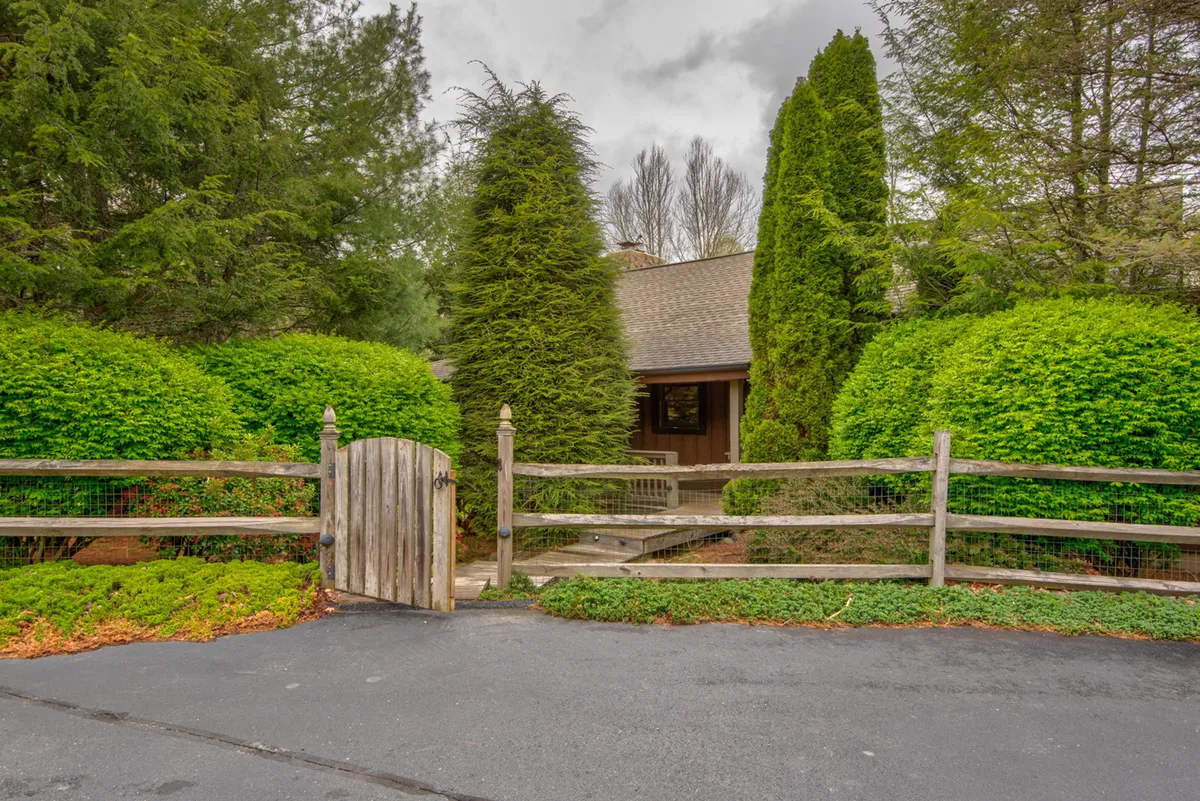 A welcoming wooden gate set in lush greenery opens onto a pathway leading towards the home. The verdant foliage and inviting entrance convey the spacious, secure outdoor area mentioned in the text, ideal for pets to roam safely.