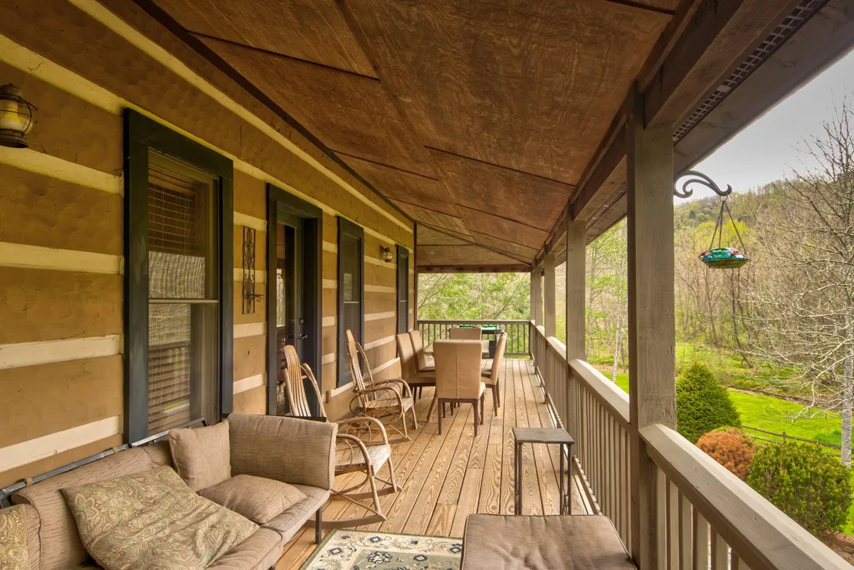 A cozy deck with comfortable seating arrangements, wooden flooring, and leafy greenery in the background. The deck is inviting for morning coffee, reading, or gathering with friends, and features safety elements suitable for pet-friendly stays.