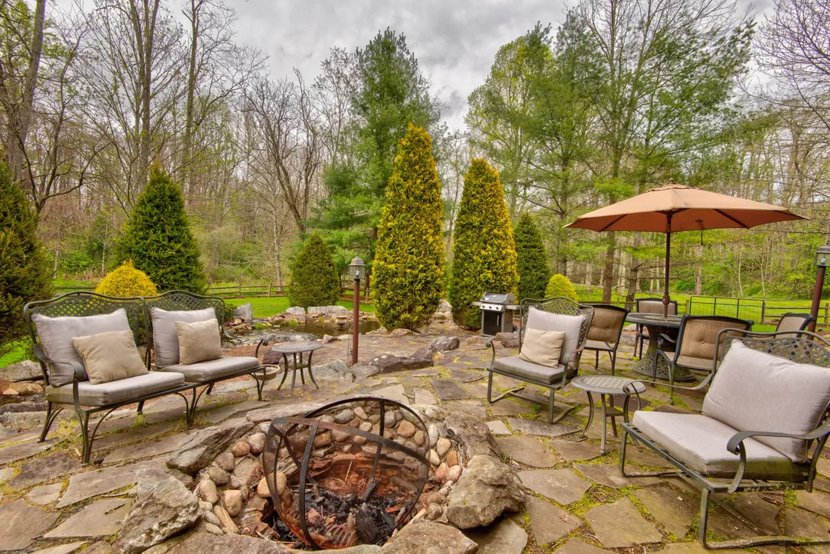 An inviting in-ground fire pit area surrounded by seating and umbrellas, set amidst green trees. The space is ideal for gathering, sharing stories, and enjoying the outdoors well into the evening.