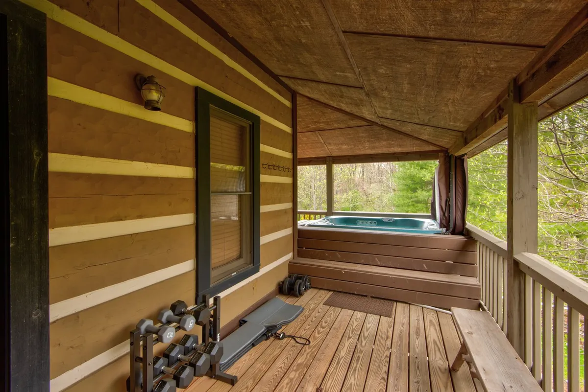 A wooden deck with a bubbling hot tub positioned to overlook the surrounding natural scenery. The space is flanked by trees and greenery, offering a tranquil, private retreat for relaxation after outdoor adventures. The deck offers ample room for post-adventure unwinding and gathering with friends.