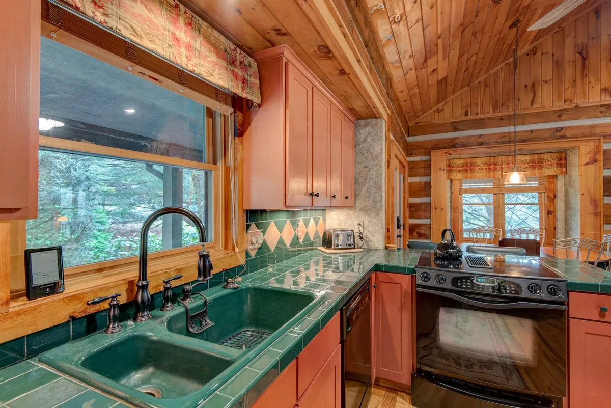 The kitchen features green tiled countertops, wooden cabinetry, a window with a view, and stainless steel appliances. The space exudes warmth and practicality, with a layout that encourages cooking family meals and gathering together.