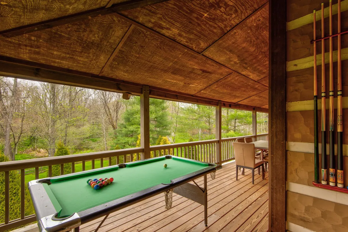 A lower-level outdoor deck features a full-sized pool table, ample seating, and panoramic views of the green landscape. Wooden railings provide safety and a sense of seclusion, while the setup encourages friendly competition and social gatherings.